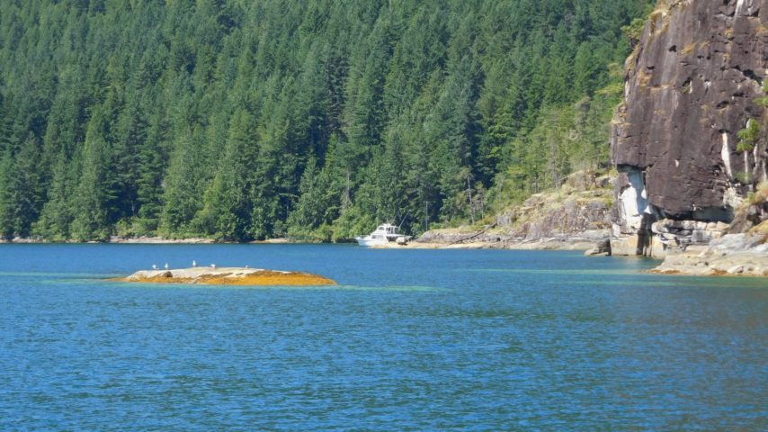 Boat anchored in cove surrounded by trees and granite cliffs in Desolation Sound