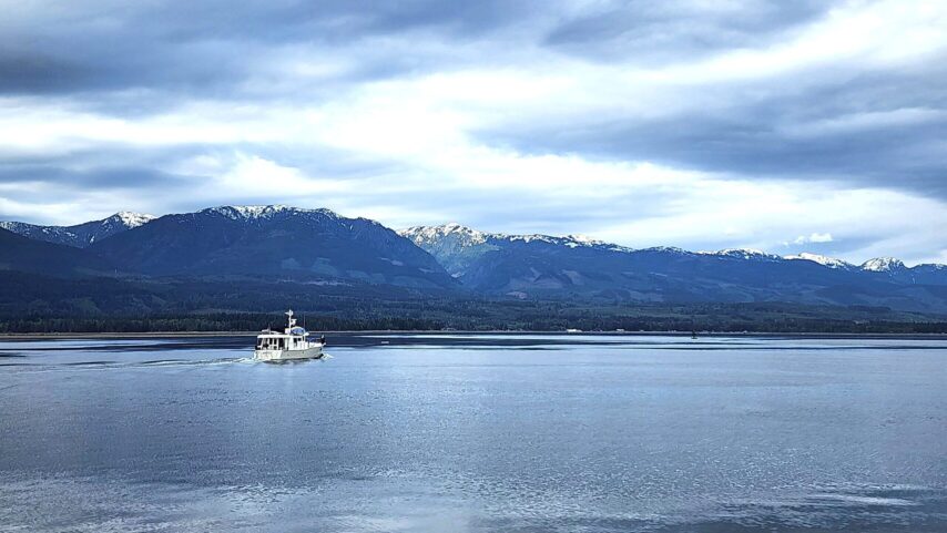 Lead boat Annie underway in calm seas with snow covered mountains in backdrop