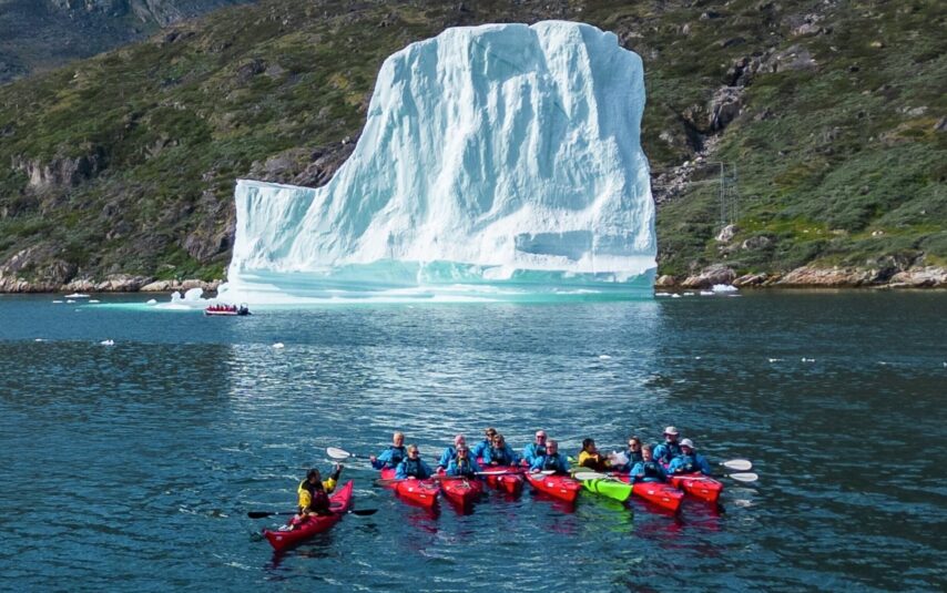 A group of kayakers in front of a large ice berg in Greenland