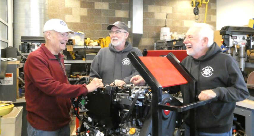 The three volunteers smiling as they work together on a marine engine